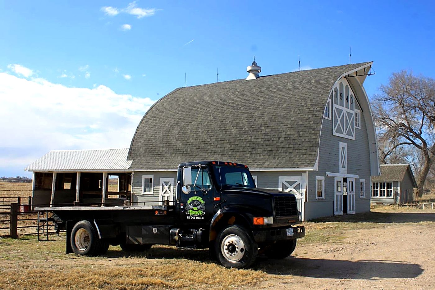 A Schank Roofing flatbed truck in front of a classic Nebraska barn